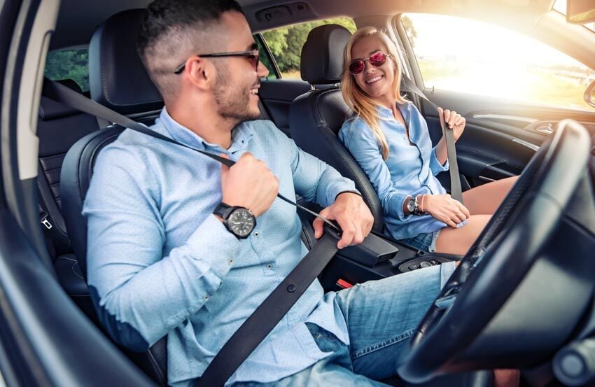 Man and woman smiling in the front two seats of a car