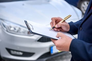 person standing in front of a car with a clipboard and pen