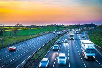 A view of motorway carriages with cars and lorries driving and a sunset in the background