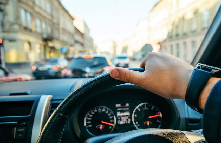 person driving a car with one hand on the steering wheel