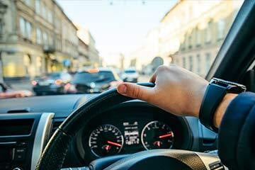 person driving a car with one hand on the steering wheel