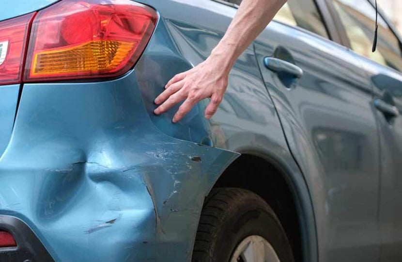 person inspecting a car bumper with a dent in it