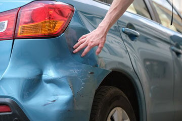 person inspecting a car bumper with a dent in it