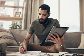 Man with tablet in one hand, taking notes with the other