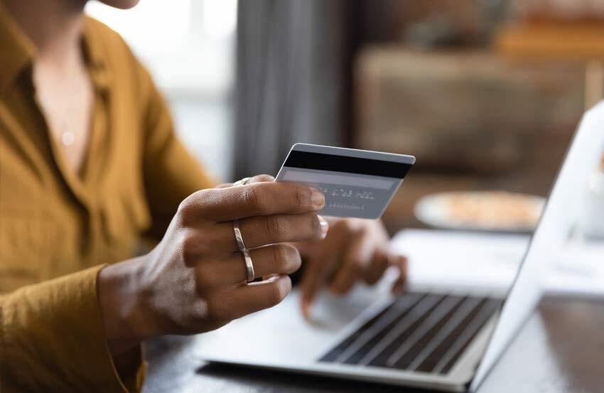 Person holding a bank card and typing their bank details into a laptop