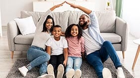 Family sat at home making a house shape with their hands