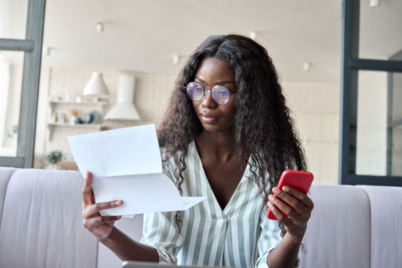 woman with mobile phone looking at bill