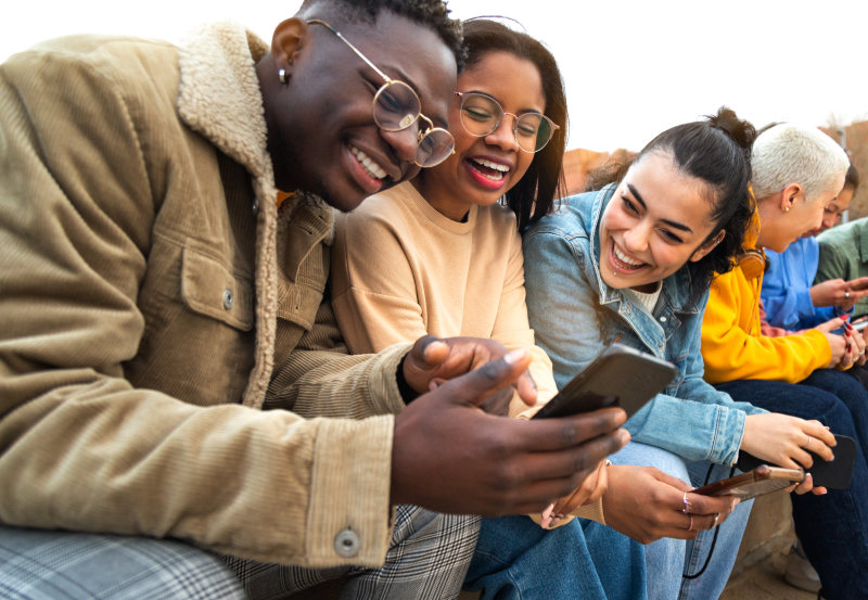 Three students smiling at something displayed on a mobile phone