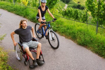 A man in a wheelchair with a woman on a bike.