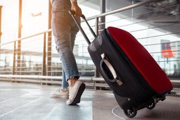 Person walking through an airport with a suitcase.