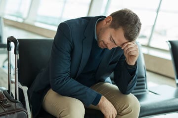 Man sat in airport lounge with a hand to his head.