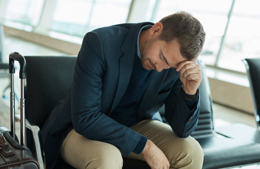 Man sat in airport lounge with a hand to his head.