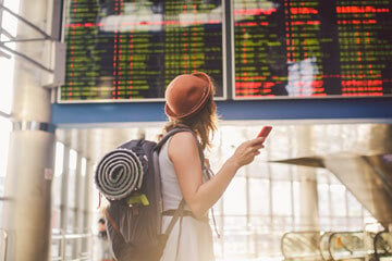 Woman holding phone looking up at transport timetable.