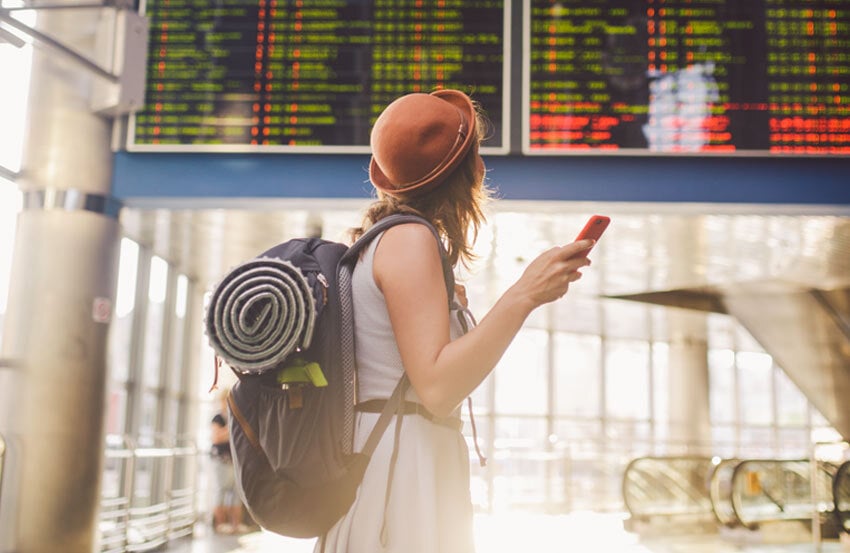 Woman holding phone looking up at transport timetable.