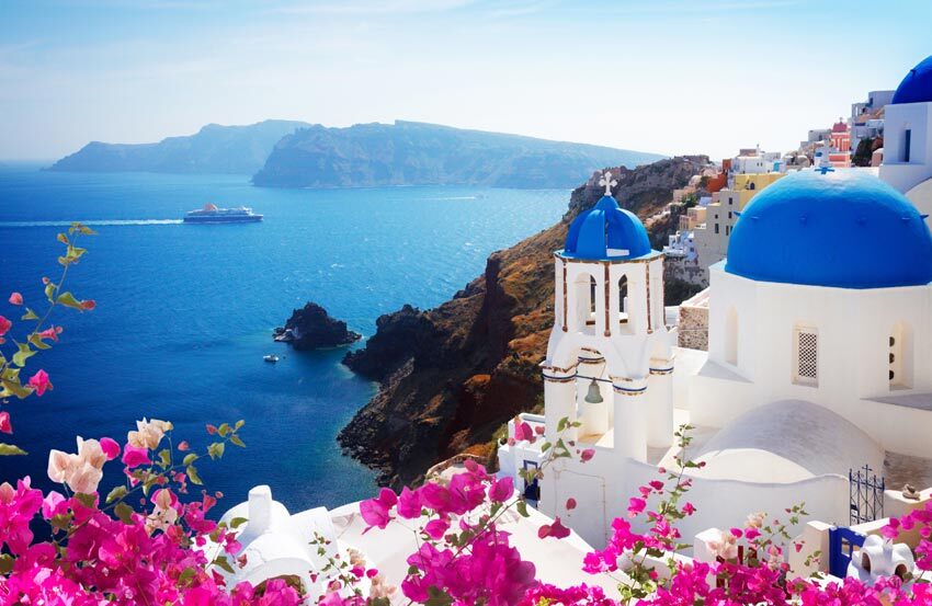 Summery view of the ocean, pink flowers, white buildings and a ship