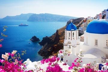 Summery view of the ocean, pink flowers, white buildings and a ship